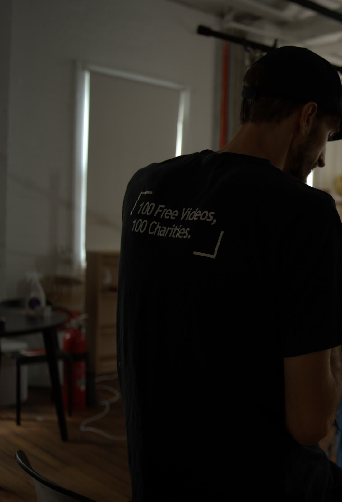 A crew member at work, the back of his shirt reading 100 Free Videos, 100 Charities.