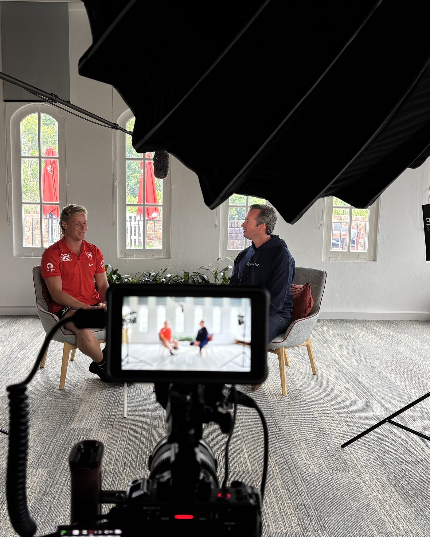 A two person interview being filmed in a bright hall, the monitor in the foreground holding the two shot.
