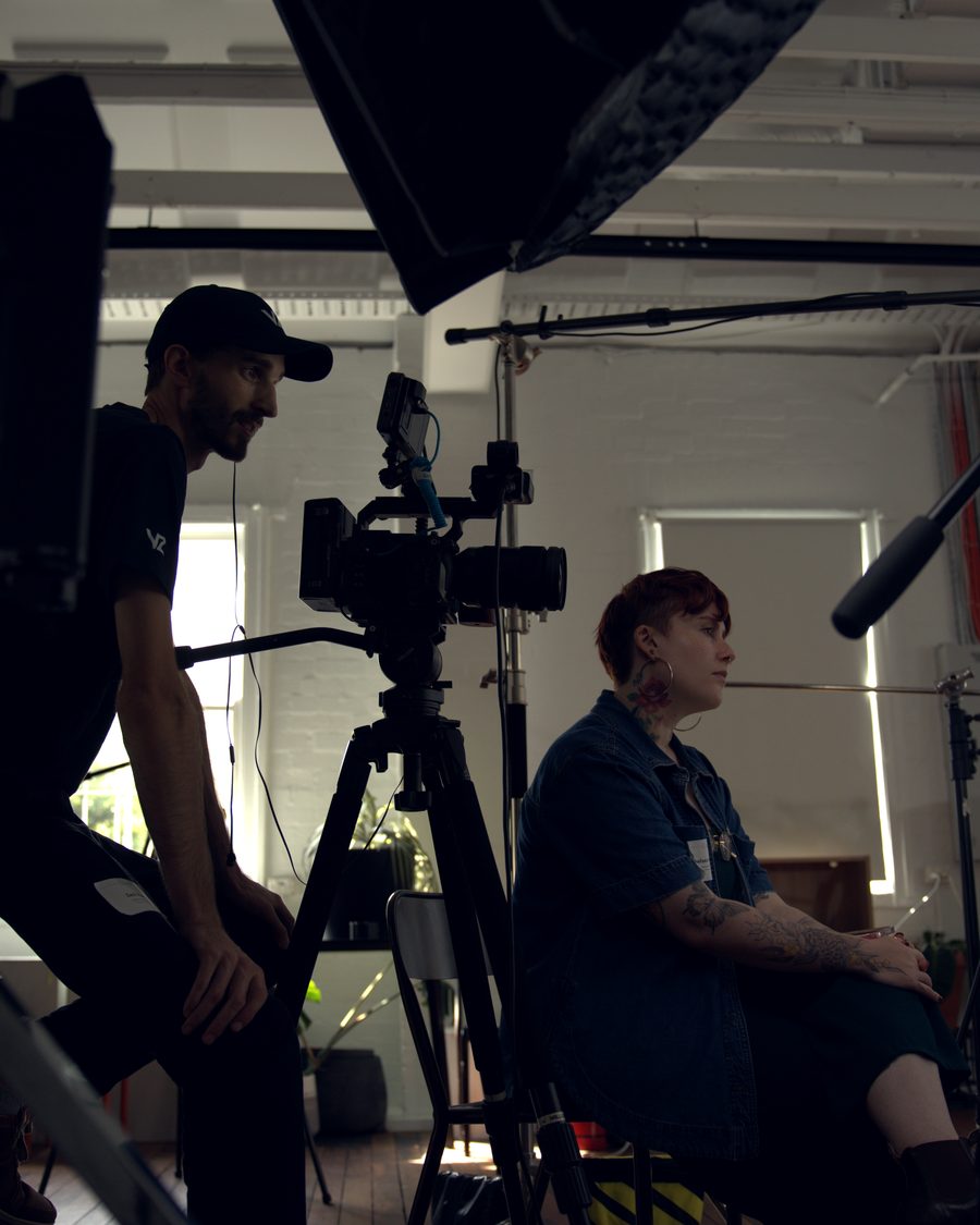 A crew member perched on a light stand, talking to the person being filmed between takes.