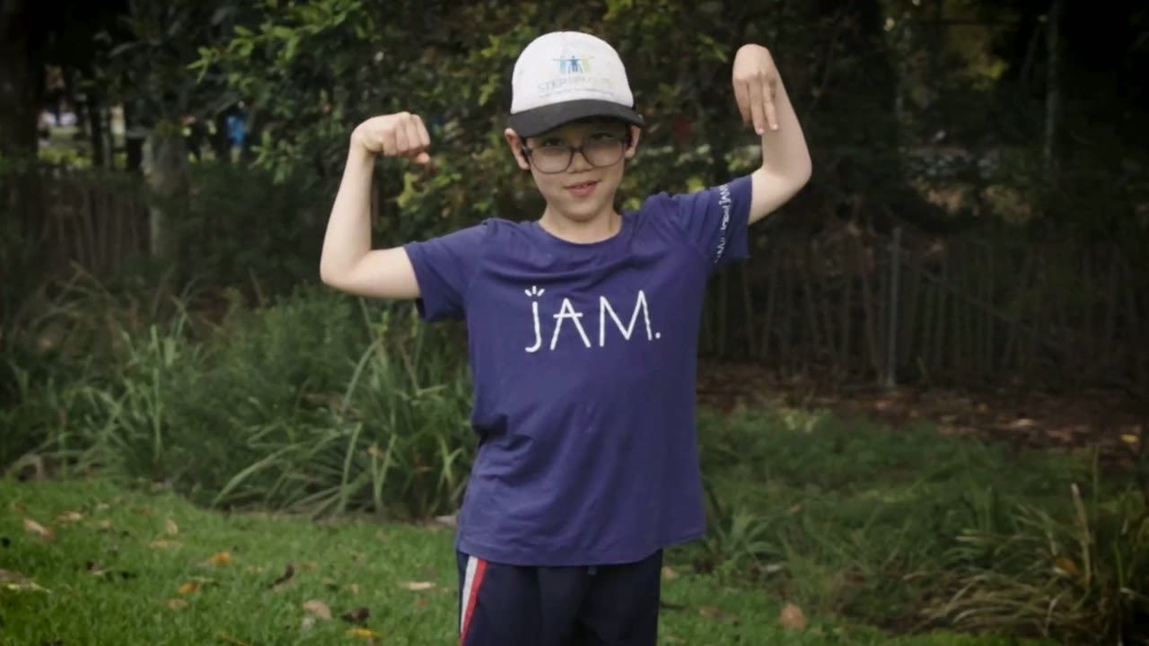 A boy flexing his arms for the camera in a park